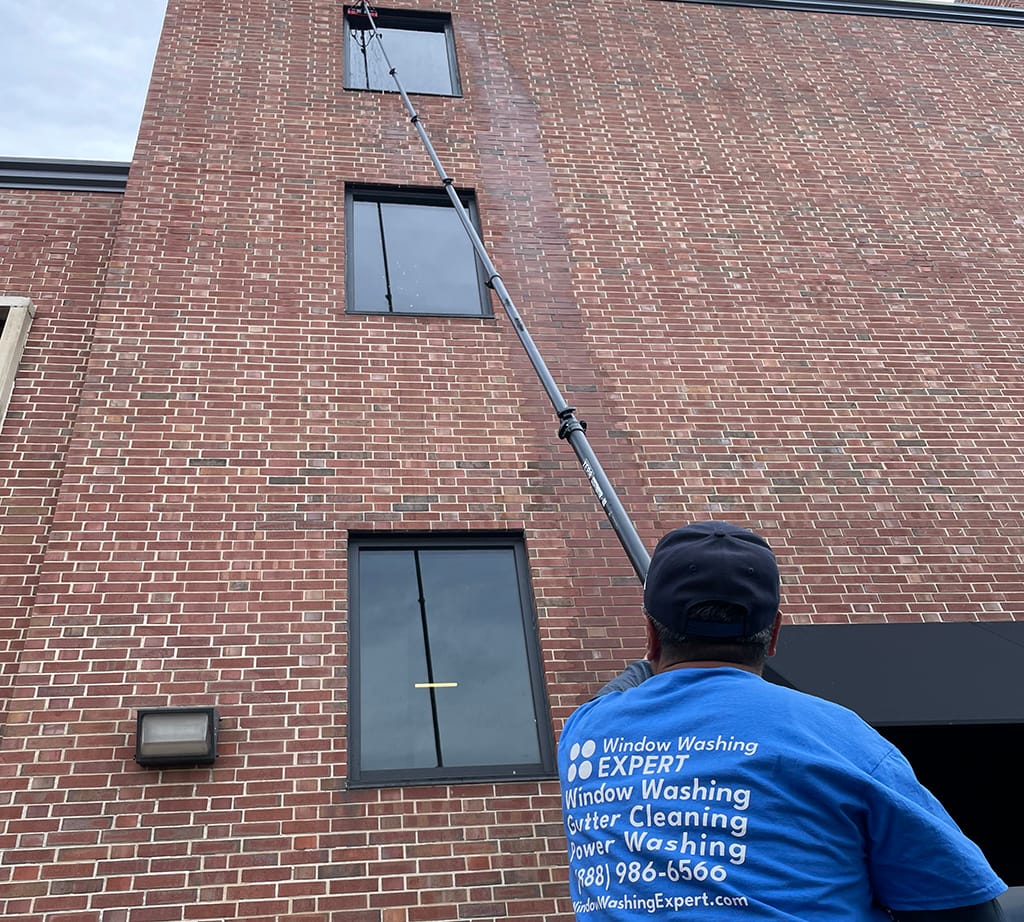 man cleaning window with water-fed poll