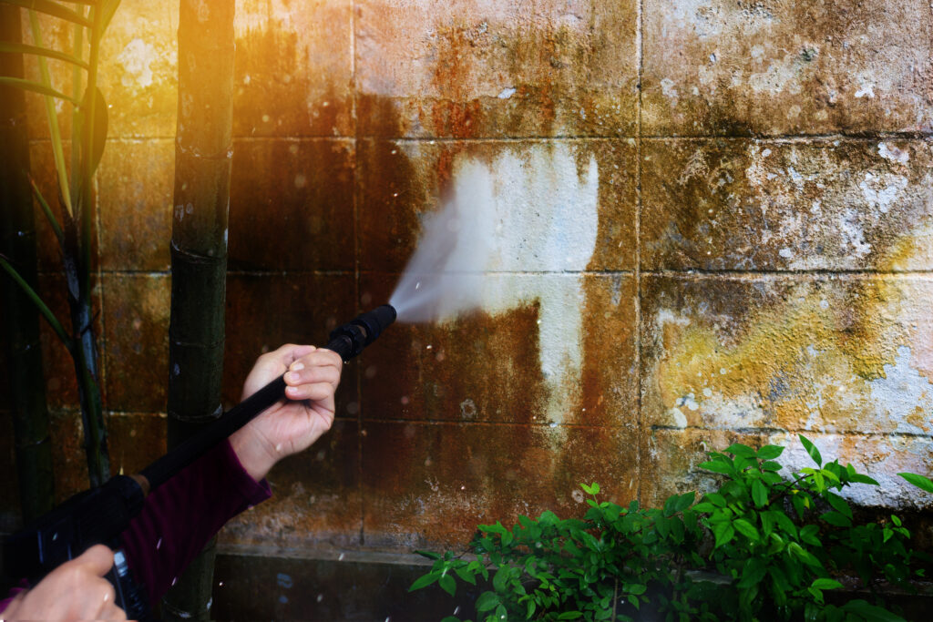 man cleaning a wall with power washer